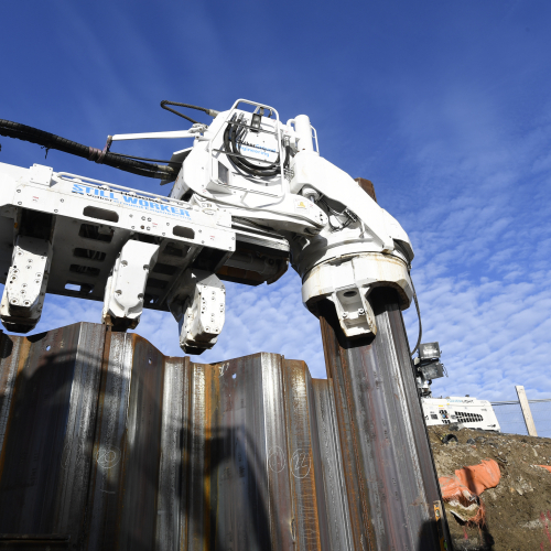 steel piling going into ground with man in Hi-vis stood on the right hand side