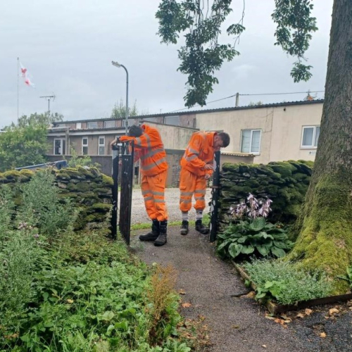 Two men in orange high vis paining an iron fence in a church yard